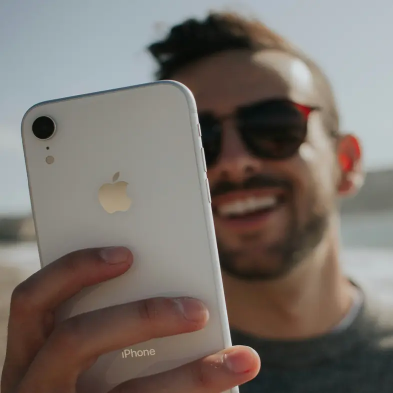 A person holding up a phone at the coast