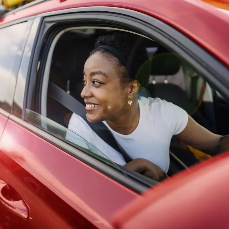 A driver smiling out of the window of a red car